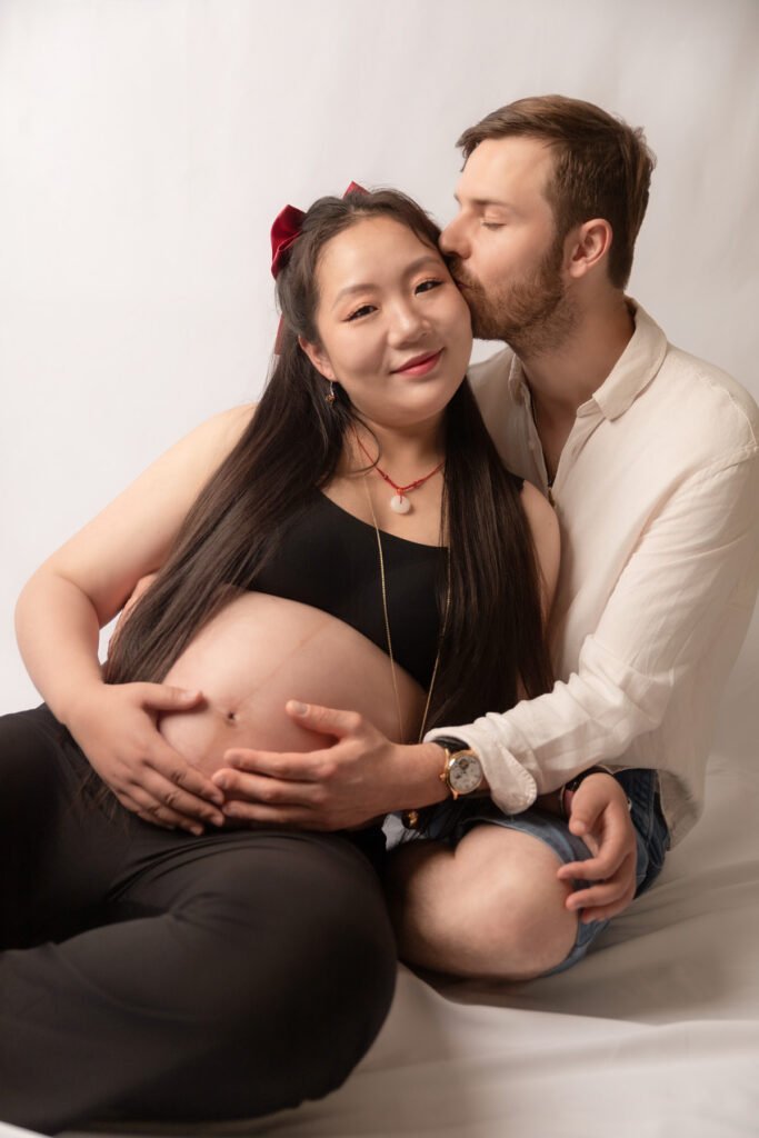 Couple assis au sol femme enceinte en studio avec la main du papa et de la maman sur le ventre grossesse