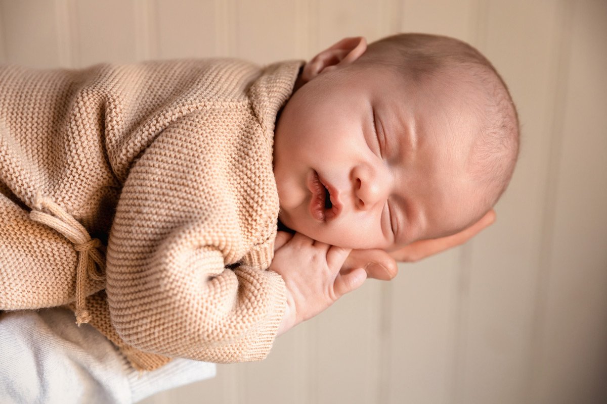 nouveau-né endormi sur le bras du papa en lumière naturelle